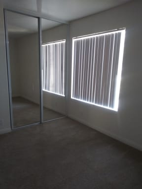 Carpeted bedroom with mirrored closet doors and large window with vertical blinds at La Costa Seashore Apartments in Carlsbad, CA