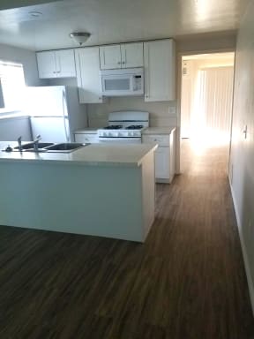Kitchen with hardwood flooring, white cabinets and appliances including gas range and microwave at Tulip Street Apartments in Escondido, California.