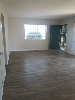 Living room with hardwood flooring, large window and front door with security screened door at Tulip Street Apartments in Escondido, California.