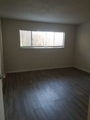 Bedroom with hardwood flooring and large window at Tulip Street Apartments in Escondido, California.