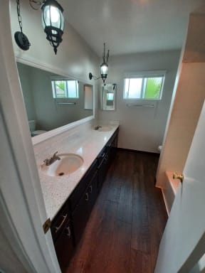 Bathroom with hardwood flooring, dark wood cabinets on double vanity and privacy window at Juniper Street Apartments in Esdondido, California.