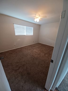 Carpeted bedroom with large double window and ceiling fan at Juniper Street Apartments in Escondido, California.