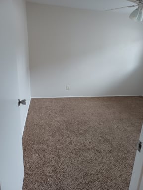 Carpeted bedroom with ceiling fan/light at Juniper Street Apartments in Escondido, California.