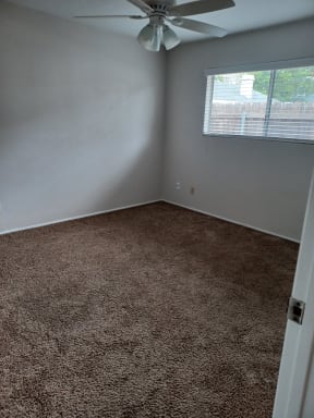 Carpeted bedroom with ceilng fan and large window at Juniper Street Apartments in Escondido, California.