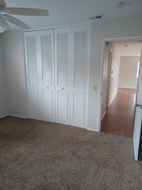 Carpeted bedroom with ceiling fan and large closets at Juniper Street Apartments in Escondido, California.