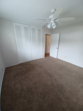 Carpeted bedroom with large closets and ceiling fan at Juniper Street Apartments in Escondido, California.