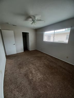 Carpeted bedroom with nice double window, ceiling fan, and walk-in closet at Juniper Street Apartments in Escondido, California.