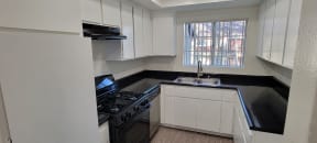 Kitchen with spacious white cabinets, gas range, and dishwasher at Northwood Apartments in Upland, California.
