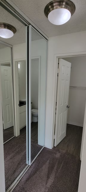 Carpeted bedroom with large mirrored door closet and private bathroom at Northwood Apartments in Upland, California.