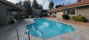 Swimming pool, sun deck chairs and tables at Sierra Vista Apartment Homes in Lake Elsinore, California.