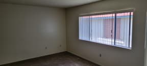 Carpeted bedroom with large window and vertical blinds at Magnolia Apartments in Riverside, California.