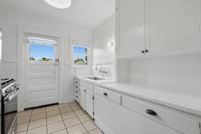 A white kitchen with a stove, sink, and cabinets.