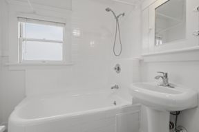 A white bathroom with a tub, sink, and mirror.