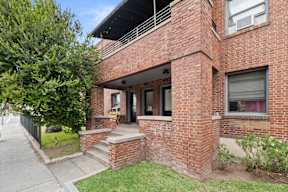 A red brick house with a black metal fence and a tree in front.