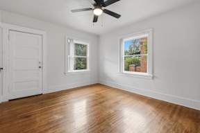 A room with a ceiling fan and two windows.