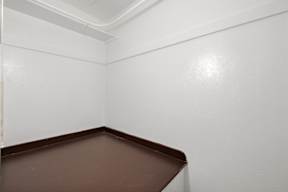 A corner of a room with white walls and brown floor.