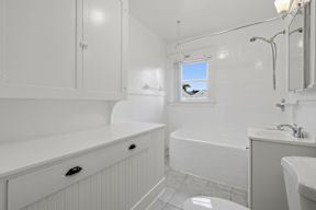 A white bathroom with a window showing a tree and a blue sky.