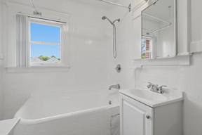 A white bathroom with a tub, sink, and mirror.