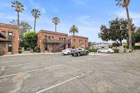 A parking lot with cars and palm trees in front of buildings.