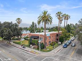 A street view with a red brick building and palm trees.