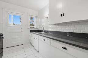 A kitchen with white cabinets and black countertops.