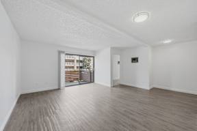 A spacious room with wooden flooring and a sliding glass door leading to a balcony.