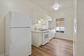 A white refrigerator stands in a kitchen with wooden floors and white cabinets.