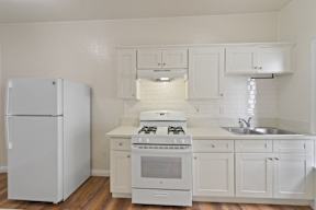 A white kitchen with a refrigerator, stove, and sink.