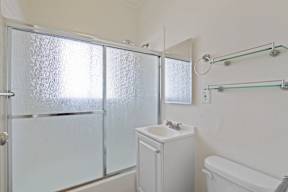 A white bathroom with a glass shower door and a white sink.