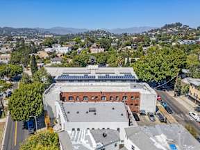 A large building with a flat roof is surrounded by other buildings and trees.