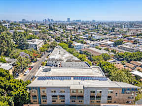 A building with solar panels on the roof is surrounded by other buildings and trees.
