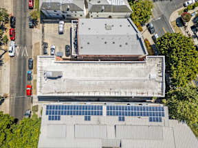 A building with solar panels on the roof is surrounded by trees and a parking lot.