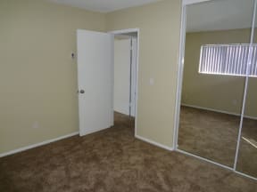 Carpeted bedroom with large window and mirrored door closets at Villa Knolls Apartments in La Mesa, California.