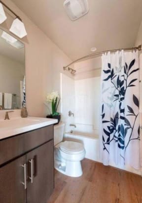 Bathroom with plank style flooring, window for natural lighting, a vanity with dark wood cabinets, and white quartz countertops at Villa Grande Apartments in San Diego, Caliornia.