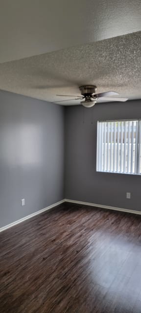 Living room with hardwood floor, ceiling fan, and lots of natural light at Grand Oaks Apartments in Lake Elsinore, California.