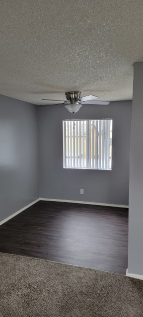 Dining room with hardwood floor, large window, and ceiling fan at Grand Oaks Apartments in Lake Elsinore, California.