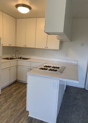 Kitchen with plank style flooring, white cabinets, and gas range at Carlsbad Sunset Senior Apartments in Carlsbad, California.