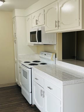 Kitchen with white cabinets and appliances, plank style flooring, and server bar at Plaza Verde Apartments in Escondido, California.