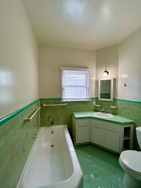 A white bathtub sits in a green tiled bathroom.