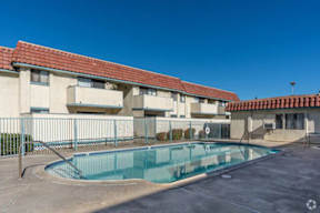 A swimming pool is located in front of a building with a red tile roof.