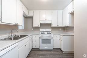 A white kitchen with a stove, sink, and cabinets.