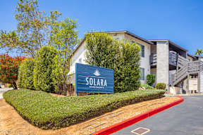 A sign for Solara Apartments is in front of a building with a red curb.