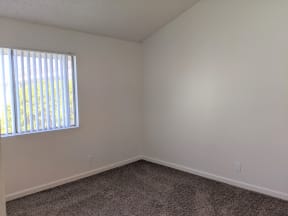 Carpeted bedroom with nice natural lighting and vertical blinds in apartment unit at the Steckel Apartments in Santa Paula, California.