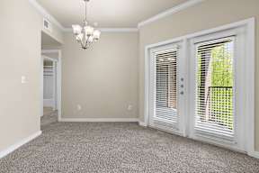 A room with a chandelier, carpeted floor, and two doors with blinds.