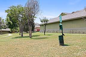 A green sign with a white number 5 on it is in the foreground of a grassy area with trees and a building in the background.