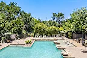 A large outdoor swimming pool surrounded by trees and lounge chairs.