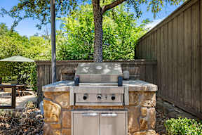 A stone and wood outdoor kitchen with a grill and oven.
