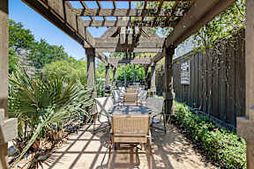 A wooden patio with a table and chairs under a pergola.