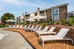 a row of white lounge chairs on a wooden deck in front of an apartment building