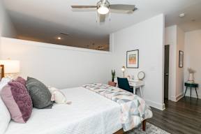 A bedroom with a bed, a desk, and a ceiling fan.